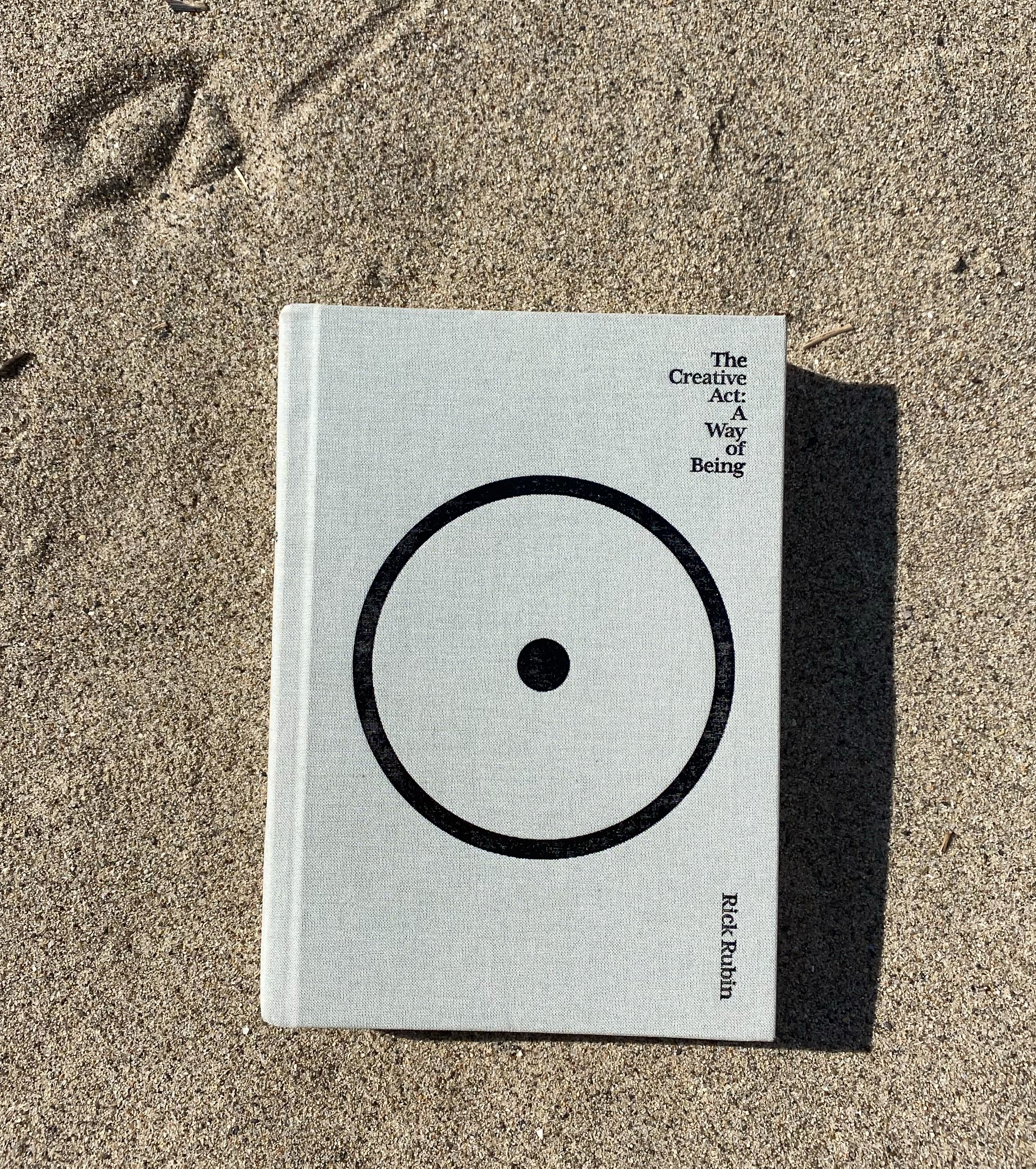 The book, The Creative Act: A Way of Being, by Rick Rubin, lying in beach sand.
